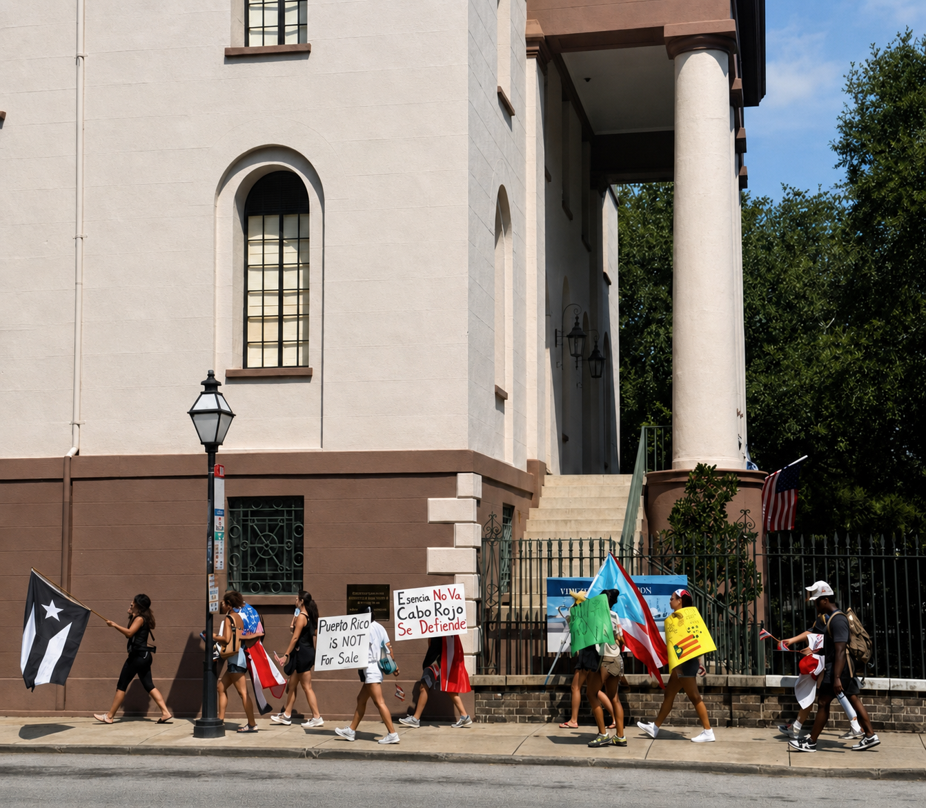 Rally participants walking past a Charleston building with Puerto Rican flags and signs.